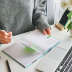 A woman working from her home office at a desk and flipping through a planner.