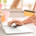 A closeup image of a woman sitting at a desk, shopping online, using a coupon site, and holding a credit card.