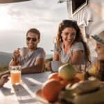 Smiling family of four enjoying breakfast at sunrise while camping