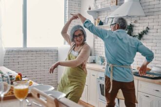 Playful senior couple in aprons dancing and smiling while preparing healthy dinner at home