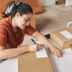 A woman online seller, writing on a shipping package label.