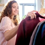 A woman standing next to a clothing rack and holding a blouse.