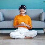 A woman sitting on the floor in her living room, wearing headphones, and getting paid to listen to music.