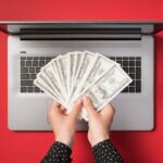 A woman's hands holding cash next to a laptop.