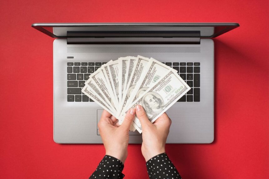 A woman's hands holding cash next to a laptop.