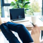 A woman working from a home office, resting her feet on her desk.