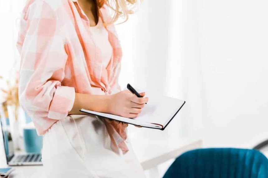 Image of woman working at home office desk and writing in a notebook