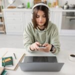 A woman working at home, sitting at her kitchen table and using her phone.