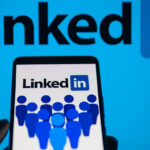 LinkedIn logo displayed on a smartphone with LinkedIn on screen seen in the background, in this photo illustration.