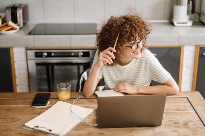 A happy, confident woman working from home on a laptop in her kitchen.