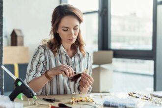 A woman sitting at a large table in her home studio, making jewelry by hand.