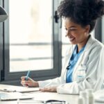 A remote medical scribe working on a laptop and taking notes.