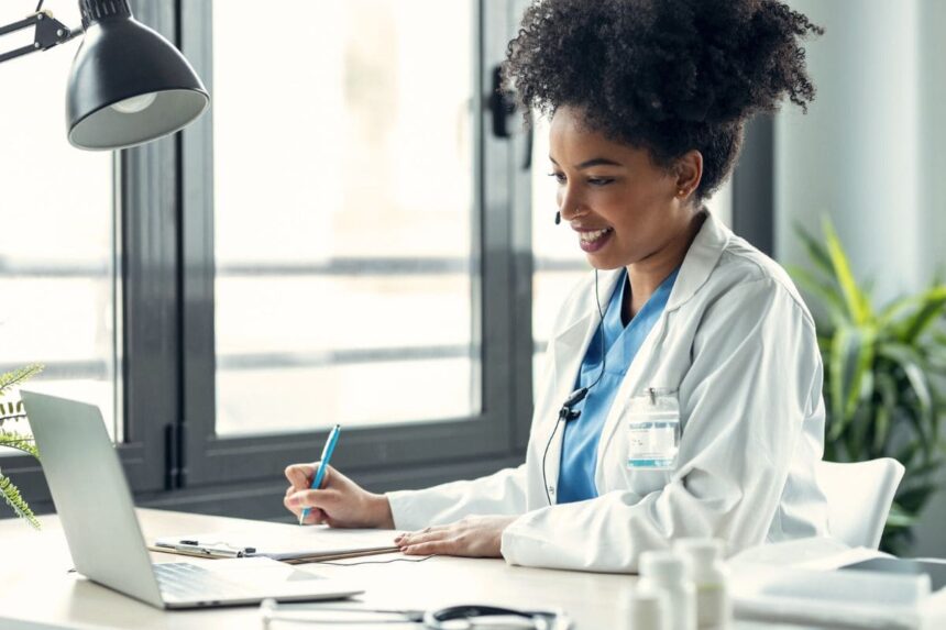 A remote medical scribe working on a laptop and taking notes.