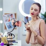 A UGC creator is sitting at a desk, showing makeup brushes to the camera while recording a video on her phone.