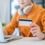 A woman listening to music and holding a Walmart gift card while using her laptop.