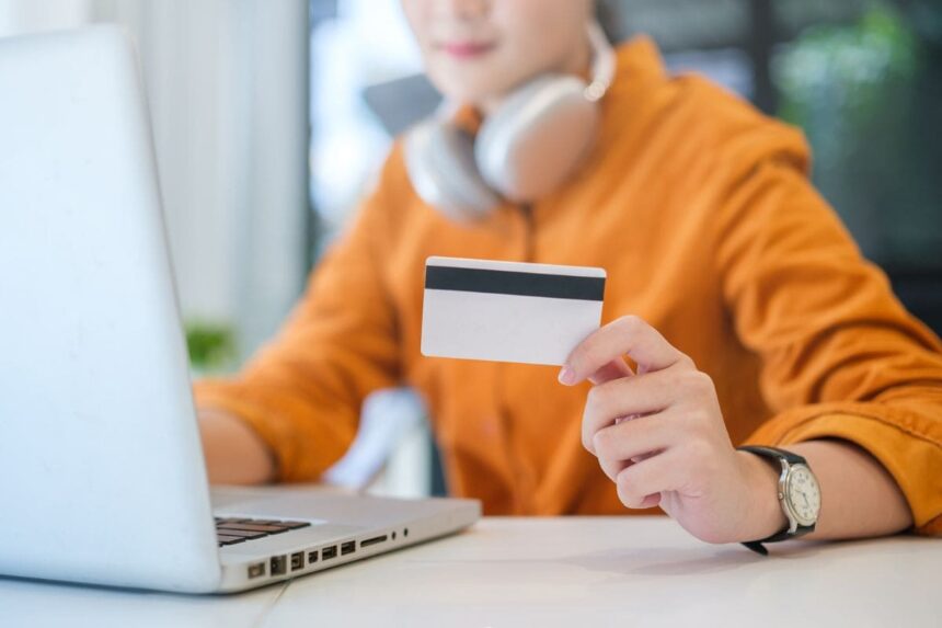 A woman listening to music and holding a Walmart gift card while using her laptop.