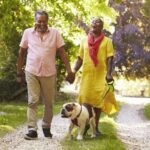 Senior Couple Walking With Pet Bulldog In Countryside