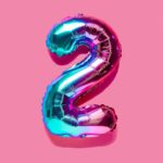 Rainbow foil balloon of the number two on pink background