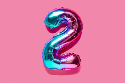 Rainbow foil balloon of the number two on pink background