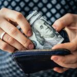 An upclose image of a woman's hands holding a wallet and counting money.