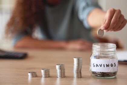 A woman counting coins in piles on a desk and then putting them into a jar labeled "savings".