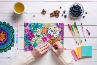 Overhead view of a woman using colored pencils to color a design in an adult coloring book.